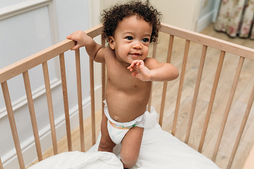 Toddler boy standing in a crib. Smiling child trying to walk.