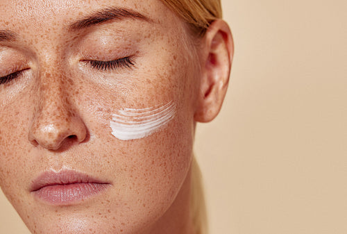 Close-up high detailed cropped shot of a young female with moisturizer on her cheek