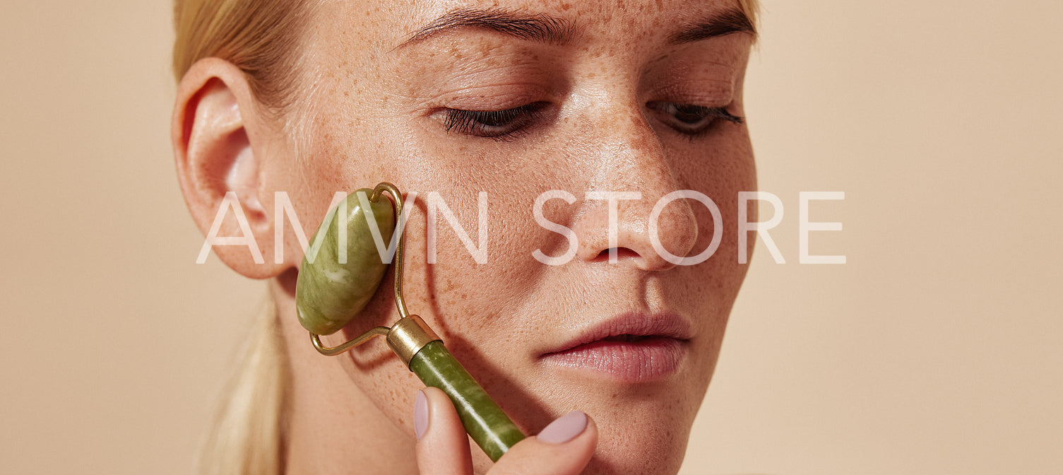 Close-up portrait of a young woman with freckles using a jade roller. Blond female doing beauty routine using face roller.