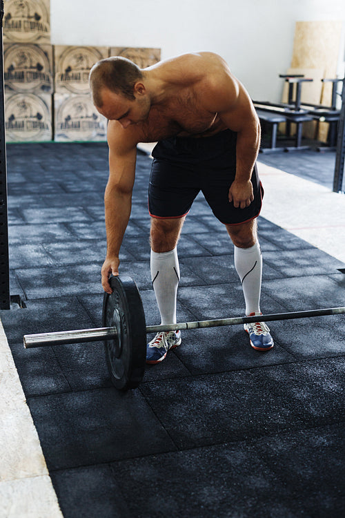 Shot of male bodybuilder adding weights to barbell, standing in sport club