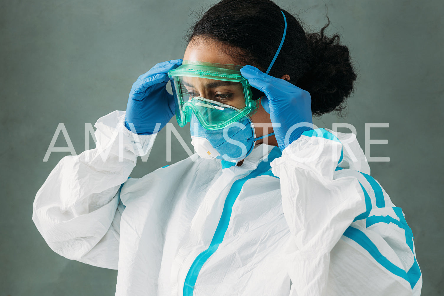 Young female medic wearing a protective suit and mask putting on goggles and looking down	