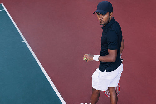 High angle of a young tennis player standing on hard court outdoors