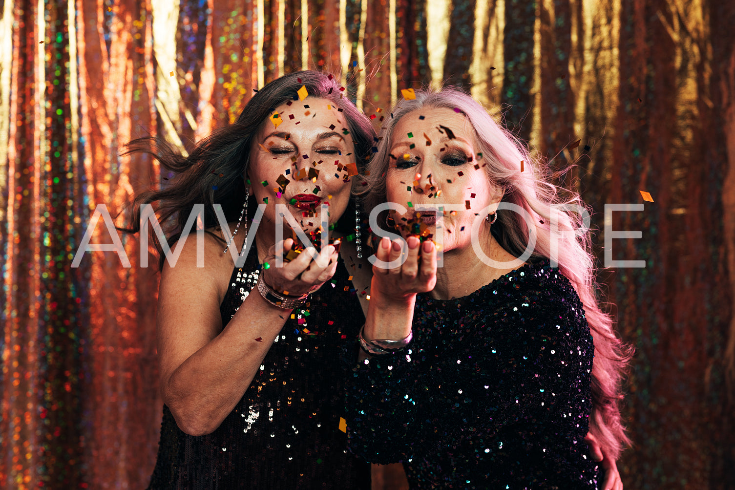 Two senior women in black dresses blowing confetti off their han