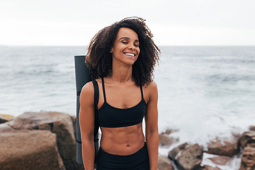 Laughing woman with closed eyes standing by the ocean after yoga training