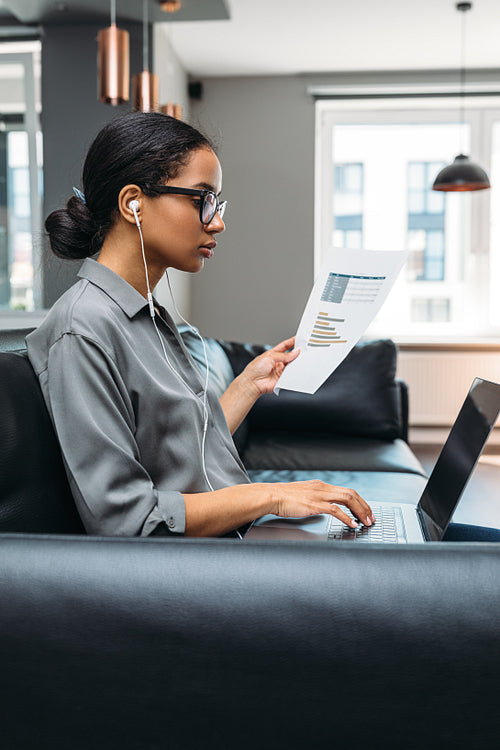 Young businesswoman working from home. Side view of freelancer using laptop computer sitting on the sofa wearing eyeglasses.