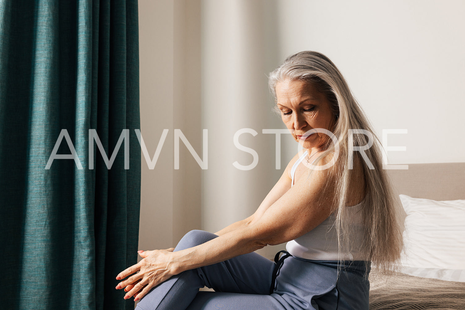 Sad and thoughtful senior woman sitting in bedroom and looking down