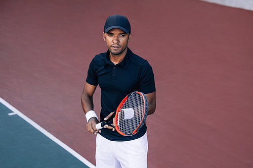 Portrait of a young tennis player with a racket standing on a hard court