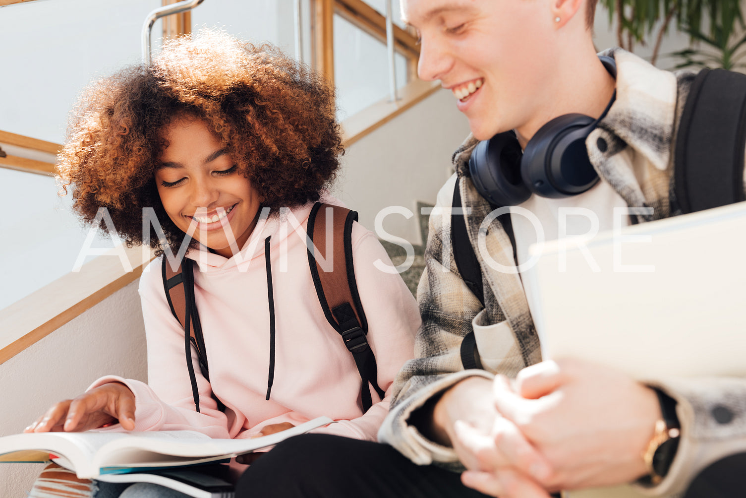 Two classmates are sitting on a stairs and reading. Boy and girl in casuals taking a break after class.