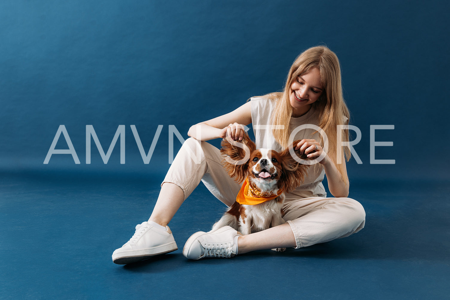 Smiling woman sitting on blue background and playing with her do