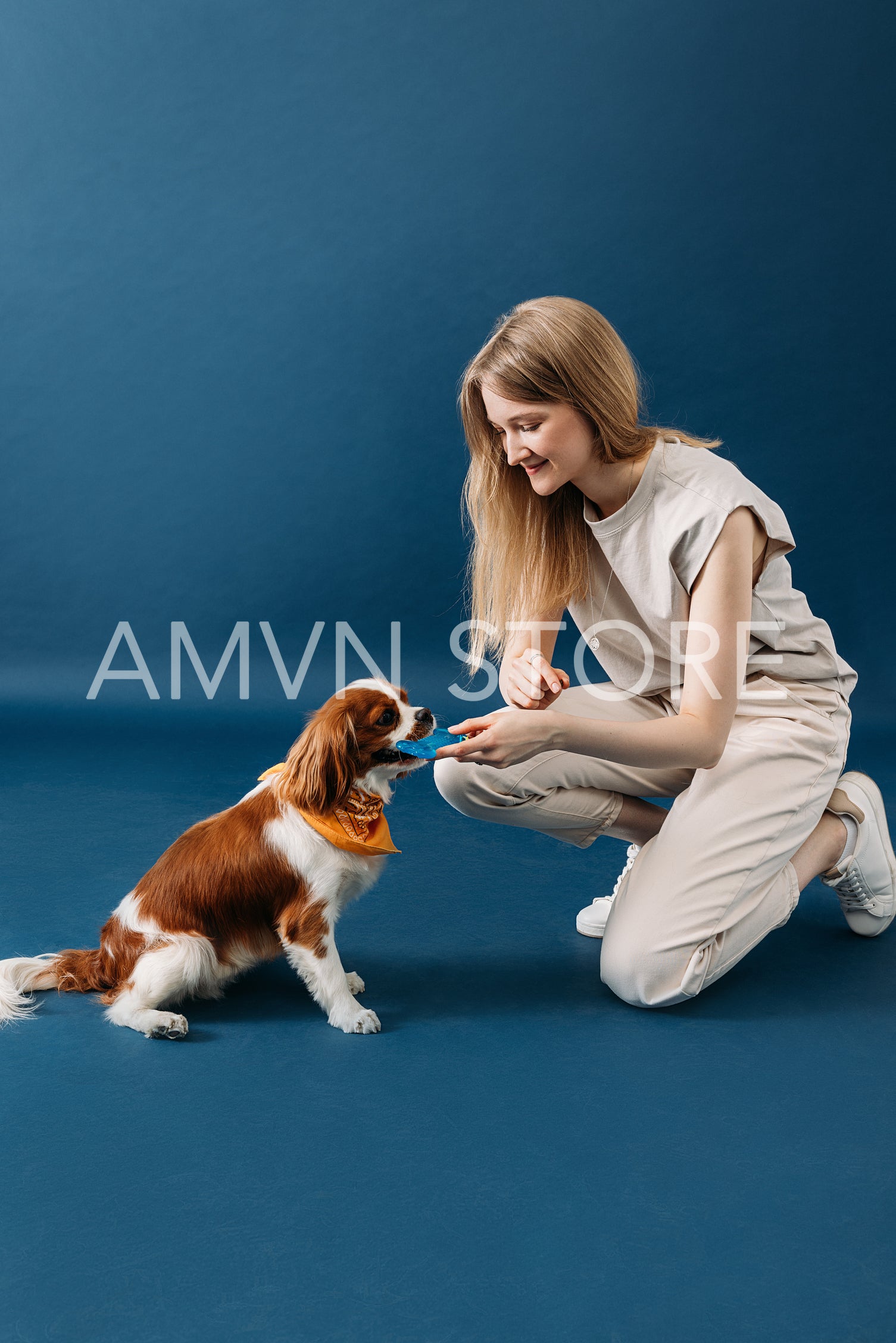 Side view of young woman playing with her dog on blue backdrop