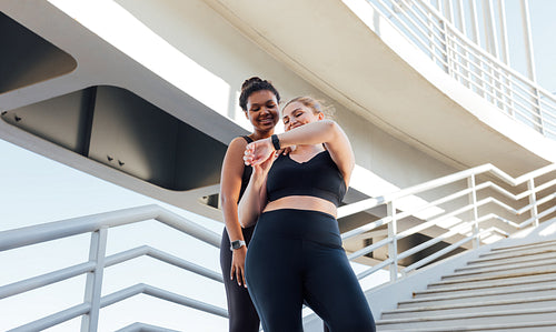 Two smiling female athletes looking at the smartwatch. Plus size female showing her fitness friend result of a workout on a smartwatch.