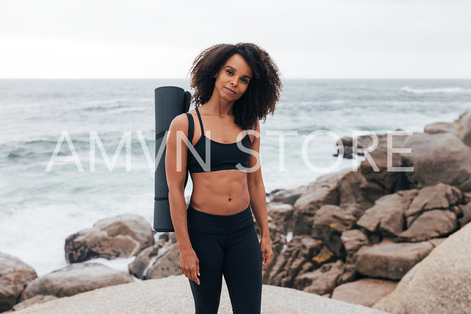 Portrait of a beautiful fit woman with yoga mat looking at camera while standing outdoors by coast