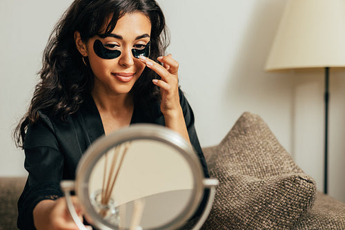 Middle east woman sitting in front of a mirror on a couch applying eye patch