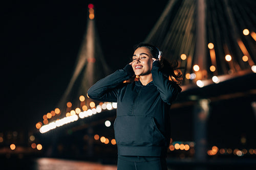 Smiling sportswoman with hands on the headphones while listening to music at night