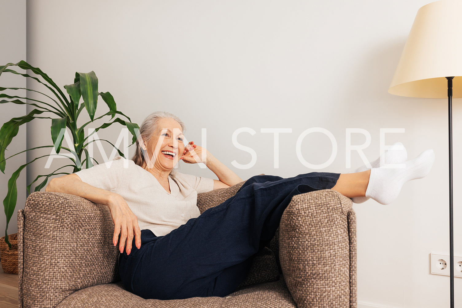 Laughing senior woman relaxing in an armchair at home. Aged female in casuals in living room.