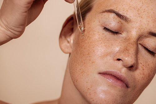 Young beautiful woman with closed eyes applying face serum with pipette