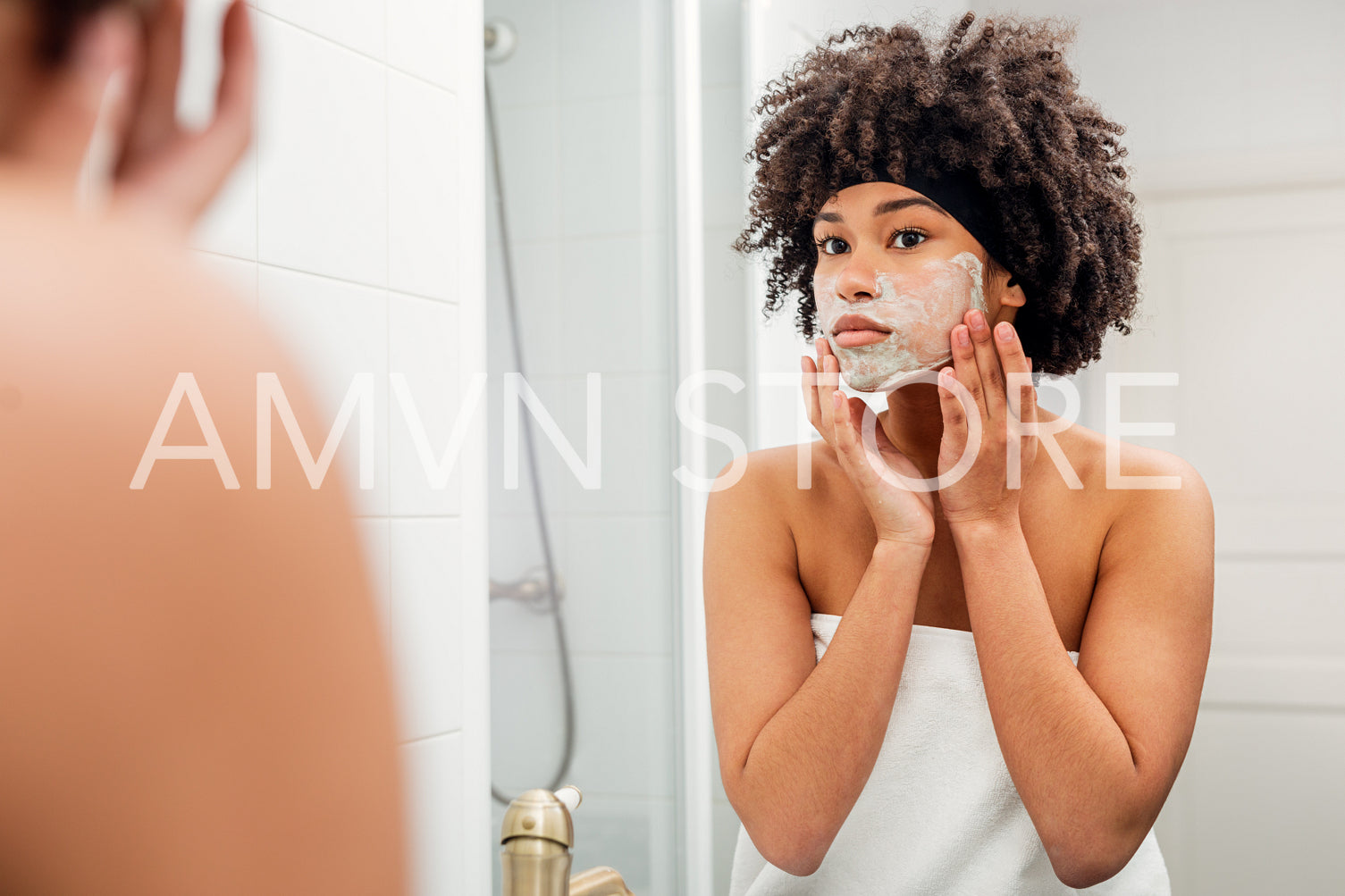 Young woman standing in front of a mirror wrapped in white towel	