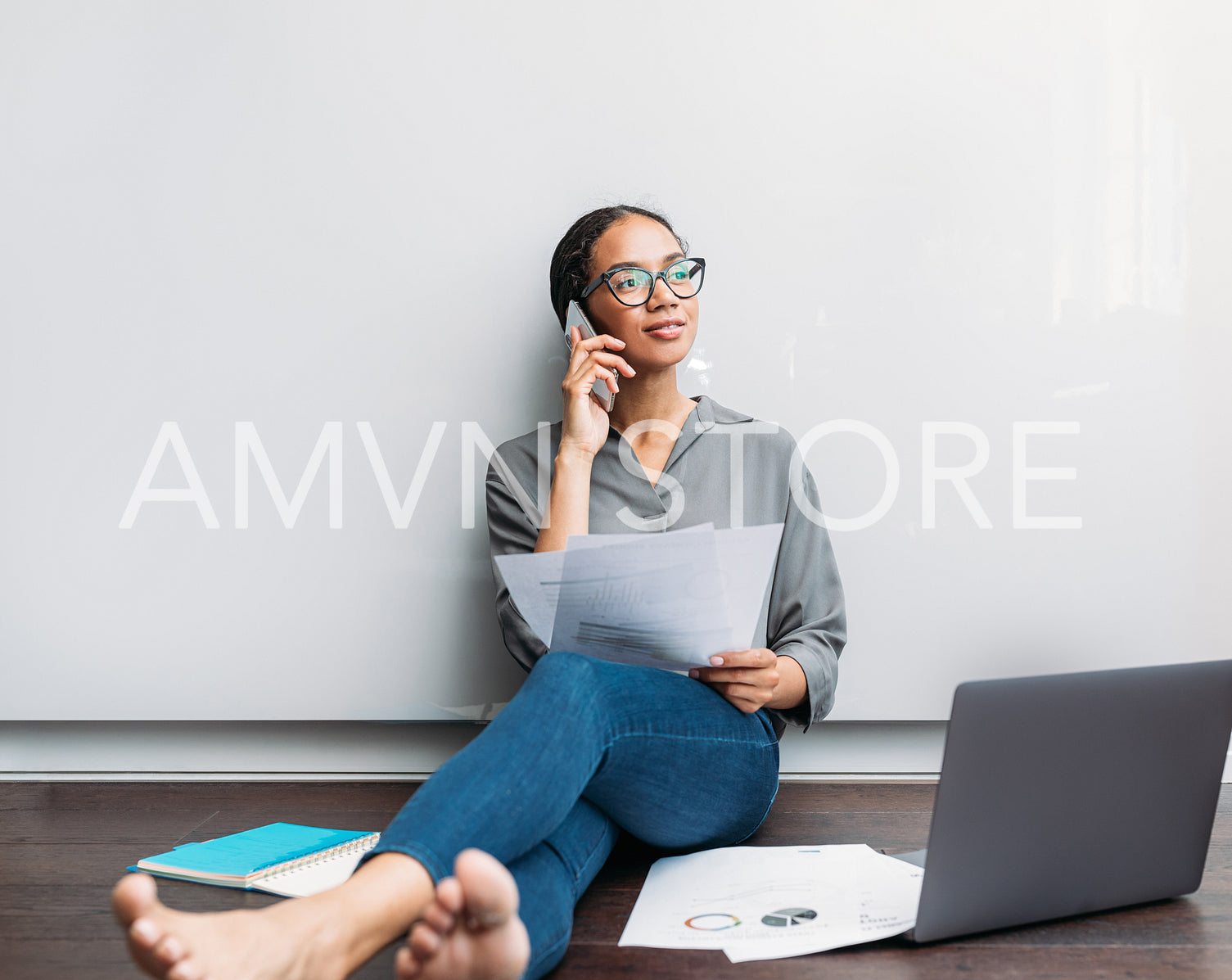 Young female with documents and a laptop sitting on a floor at home