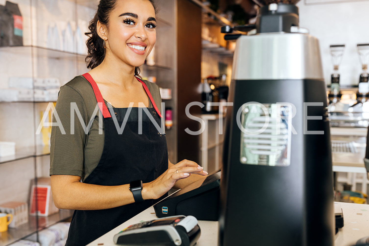 Young beautiful barista standing at counter in cafeteria and looking away	