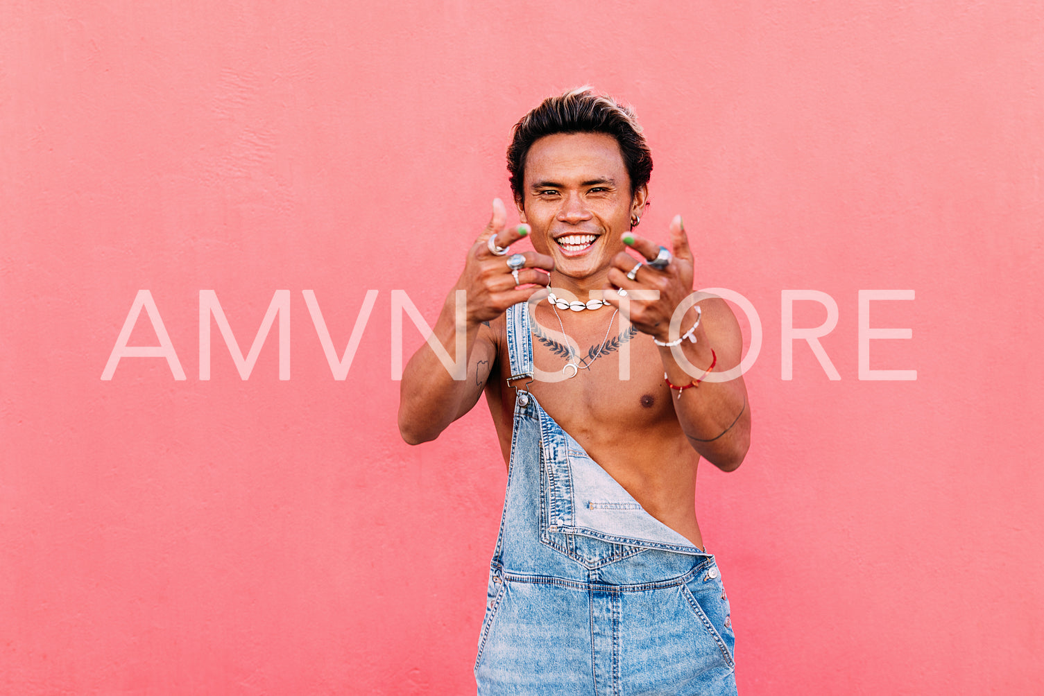 Young stylish guy in casuals dancing at pink wall and looking at camera