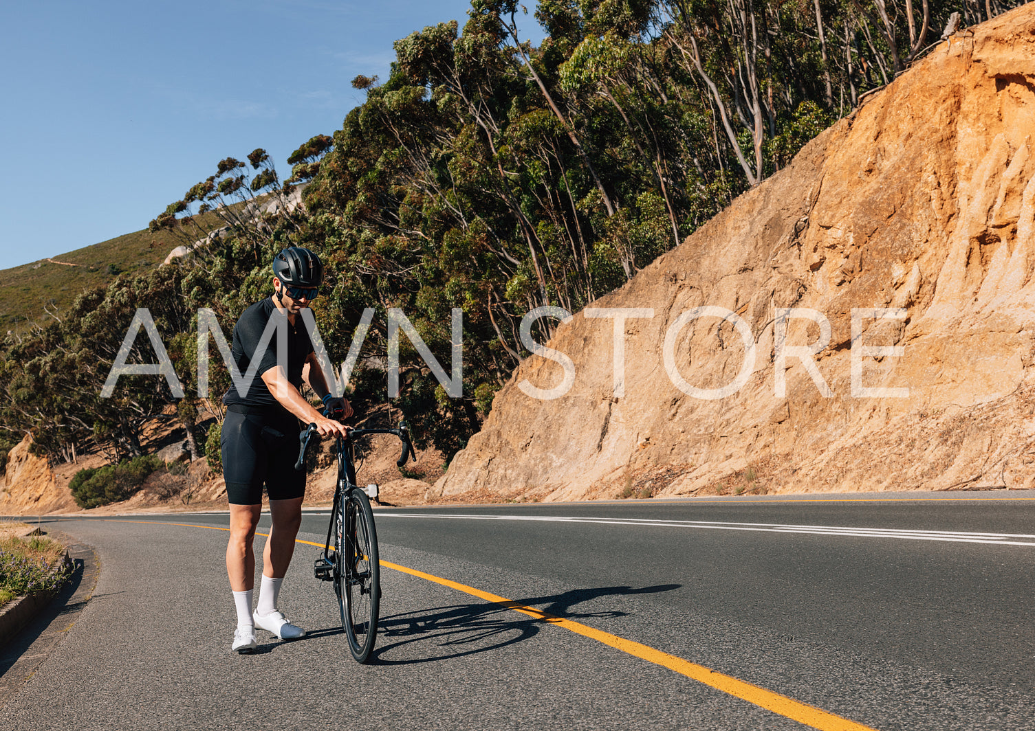 Male cyclist inspecting his bicycle while standing on a roadside on an empty road