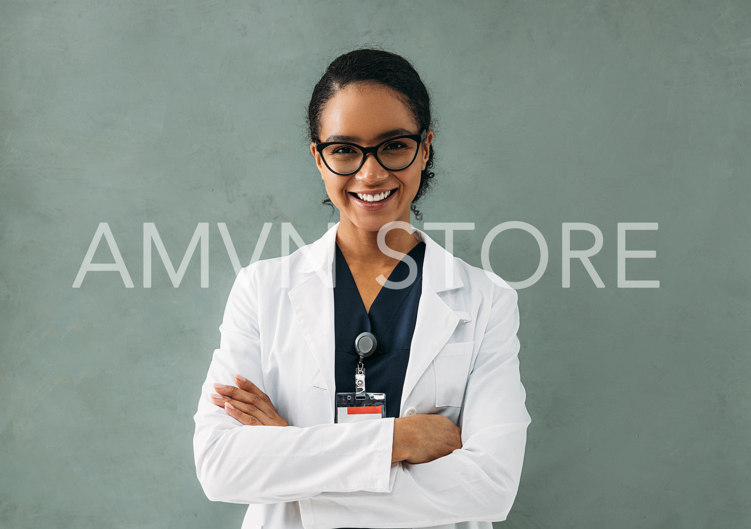 Portrait of a happy doctor in a white lab coat standing with crossed arms looking at camera at a concrete wall	