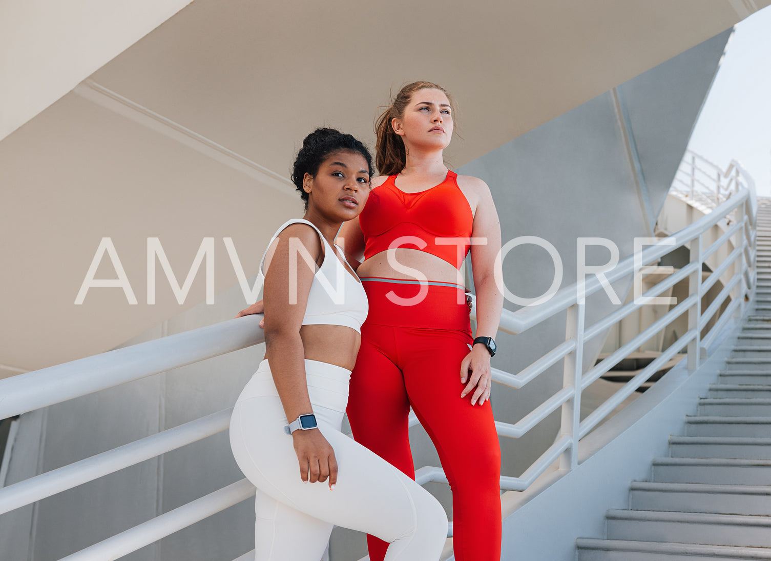 Two plus size females in sportswear standing on a staircase. Young women relaxing after exercises outdoors.