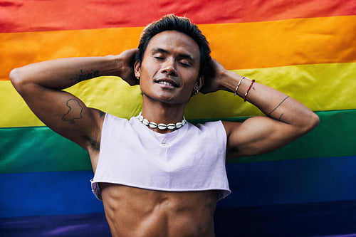 Young stylish man standing against rainbow flag with closed eyes