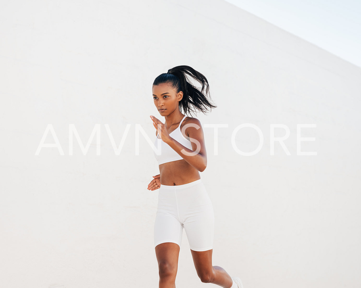 Confident woman sprinting against a white wall. Slim jogger in white fitness attire running outdoors.