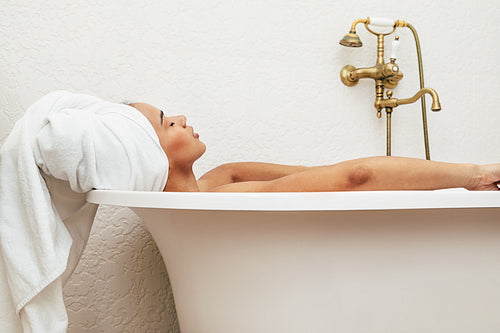 Woman in towel wrapped around head relaxing in bath