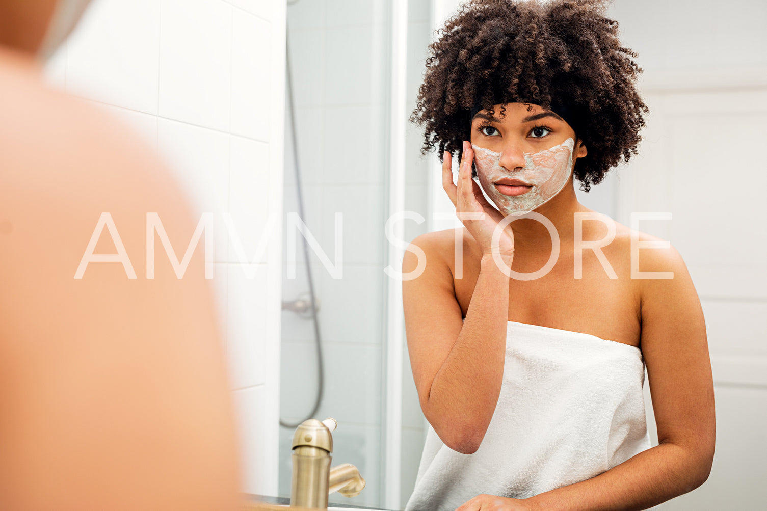 Young woman wrapped in white towel applying natural mask on her face	