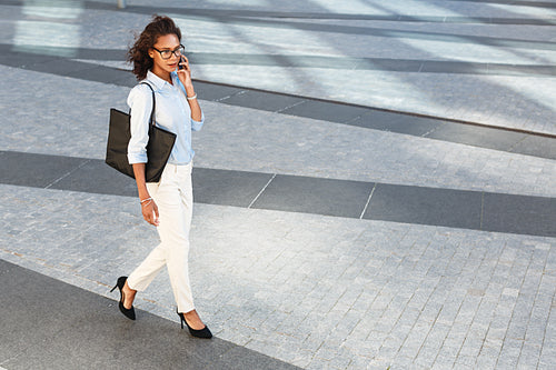 High angle view of woman in formal clothes walking outdoors and talking on smartphone