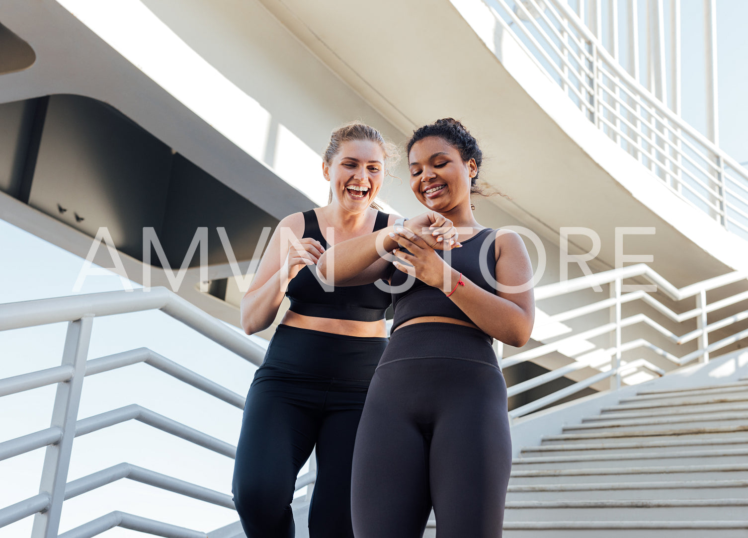 Two happy plus-size females looking at smartwatch while going down on stairs