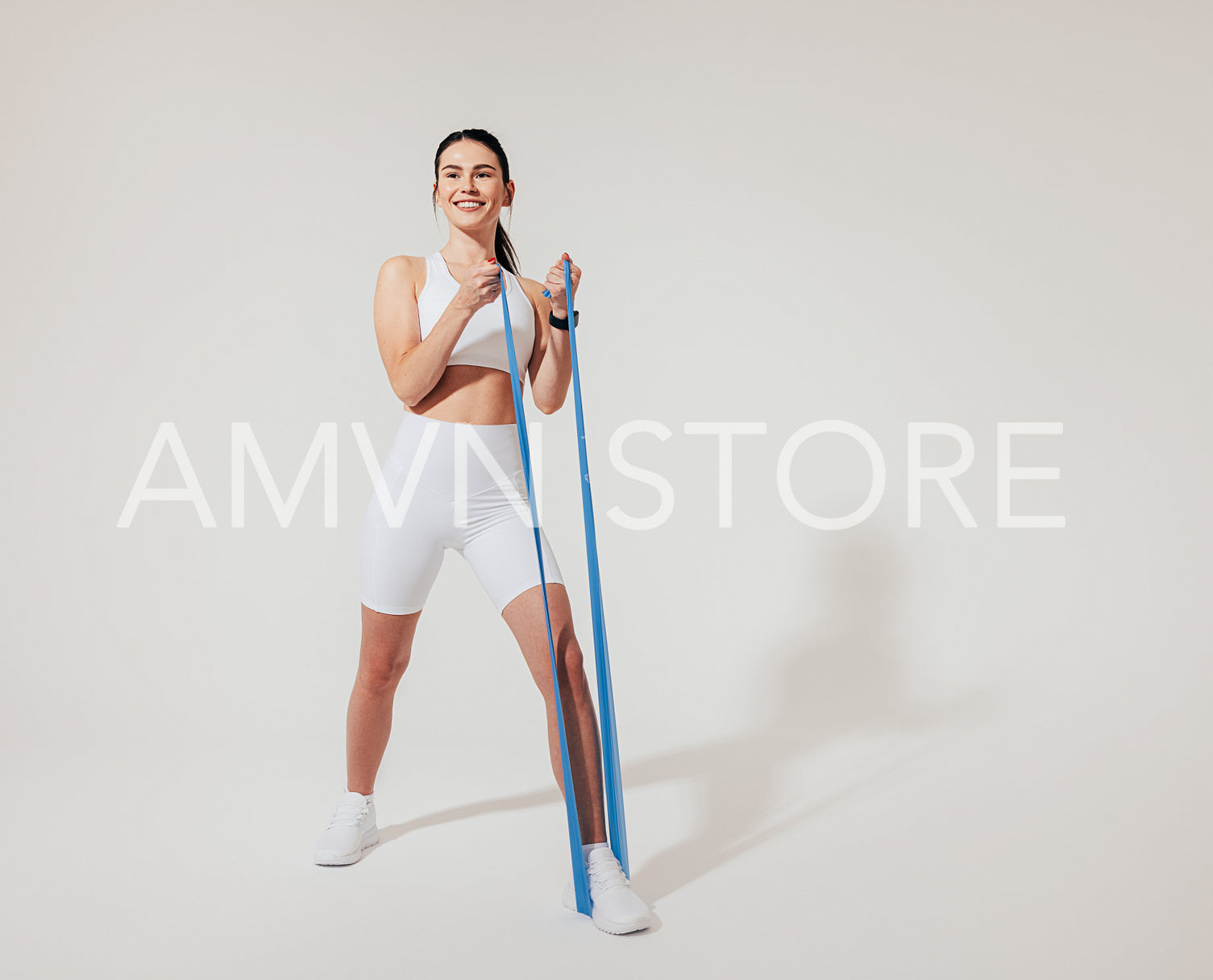 Full length of a smiling slim woman warming up with a resistance band over a white background