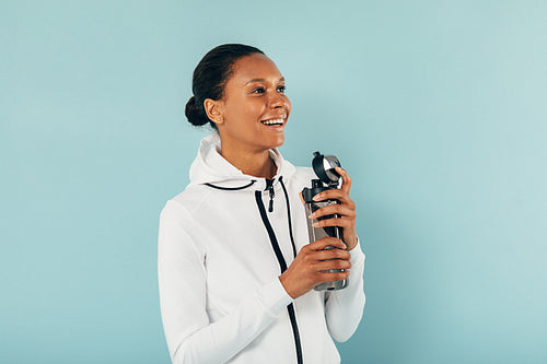 Happy woman in sports clothes holds a water bottle and looking away in studio over blue background