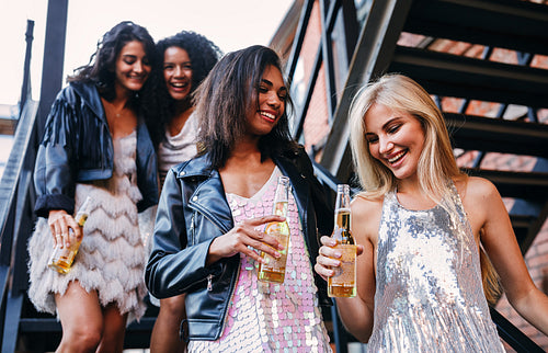 Group of young woman holds bottles of beer while stepping down on the stairs