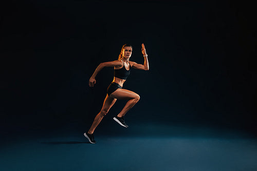 Young woman starting to run. Strong female athlete running on black background.