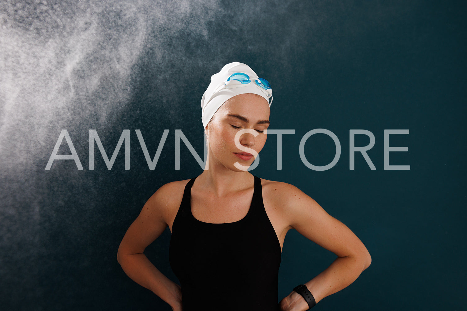 Professional female swimmer wearing a white swimming cap and goggles standing with closed eyes against blue backdrop