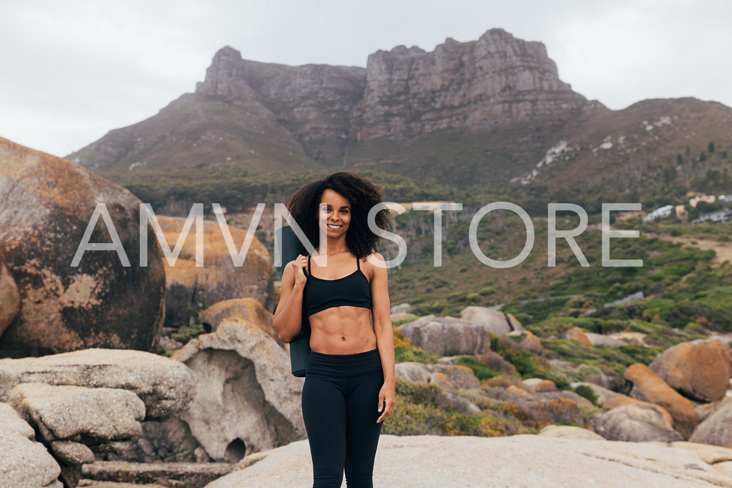 Slim woman in sportswear with yoga mat standing against beautiful landscape looking location for a evening training