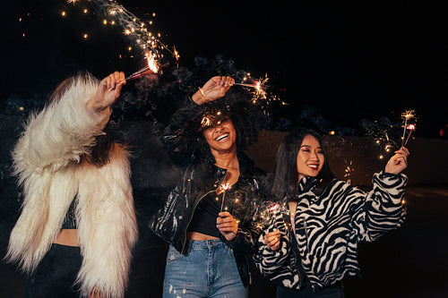 Three happy girls waving sparklers while walking together at night