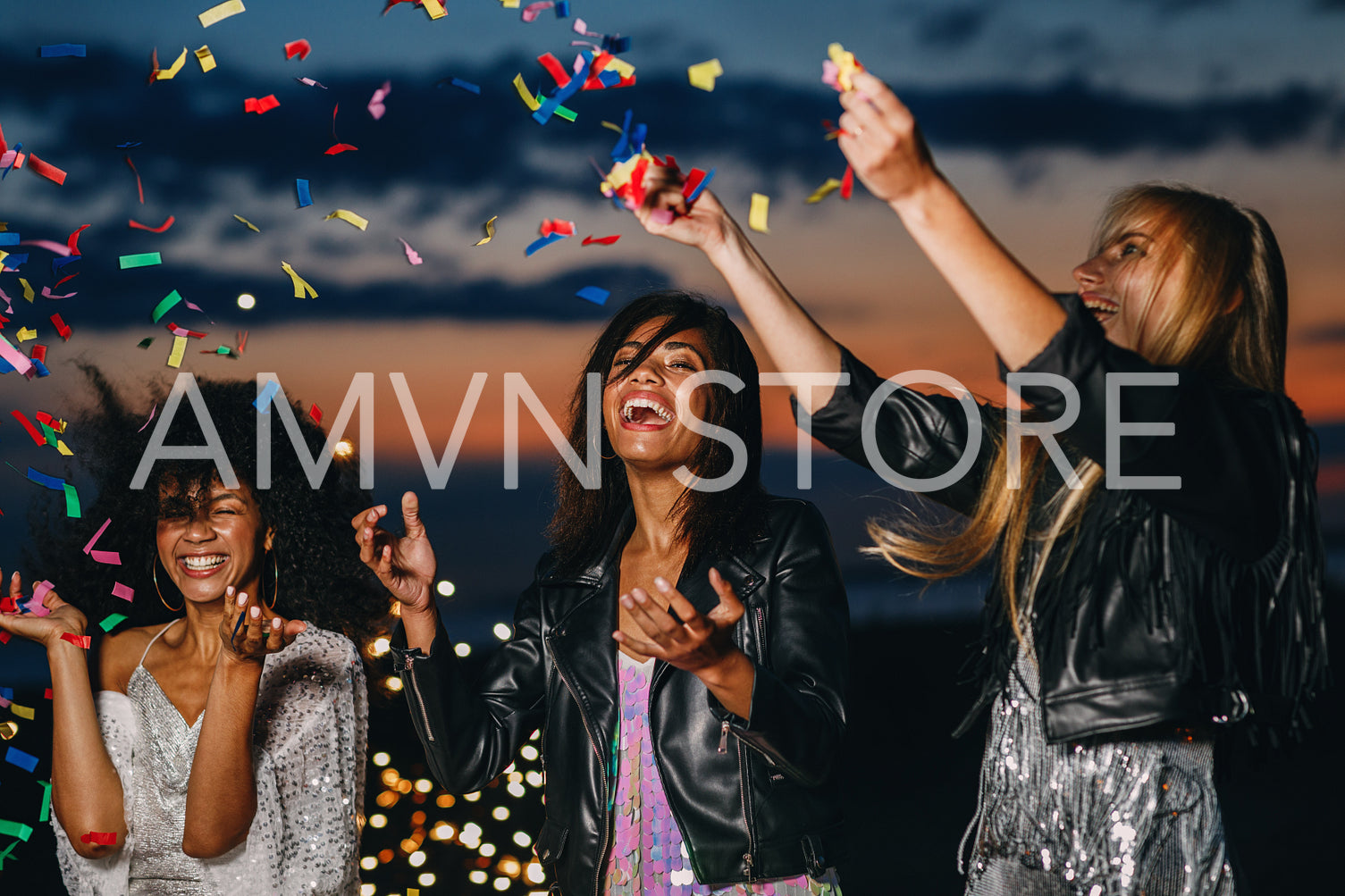 Laughing women throwing confetti at sunset. Three smiling friends having fun together.	