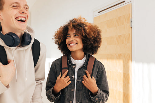 Two laughing teenagers in college. Smiling girl looking at her classmate in corridor.