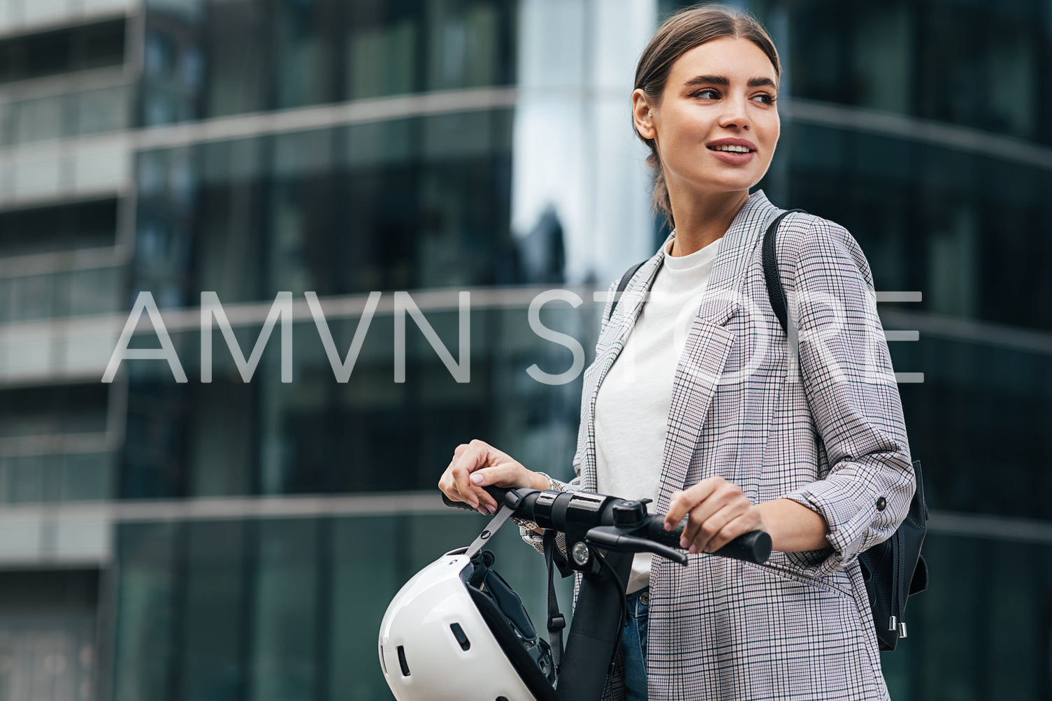 Portrait of a caucasian businesswoman with an electrical scooter. Smilaing female holding a scooter looking away in front of an office building.