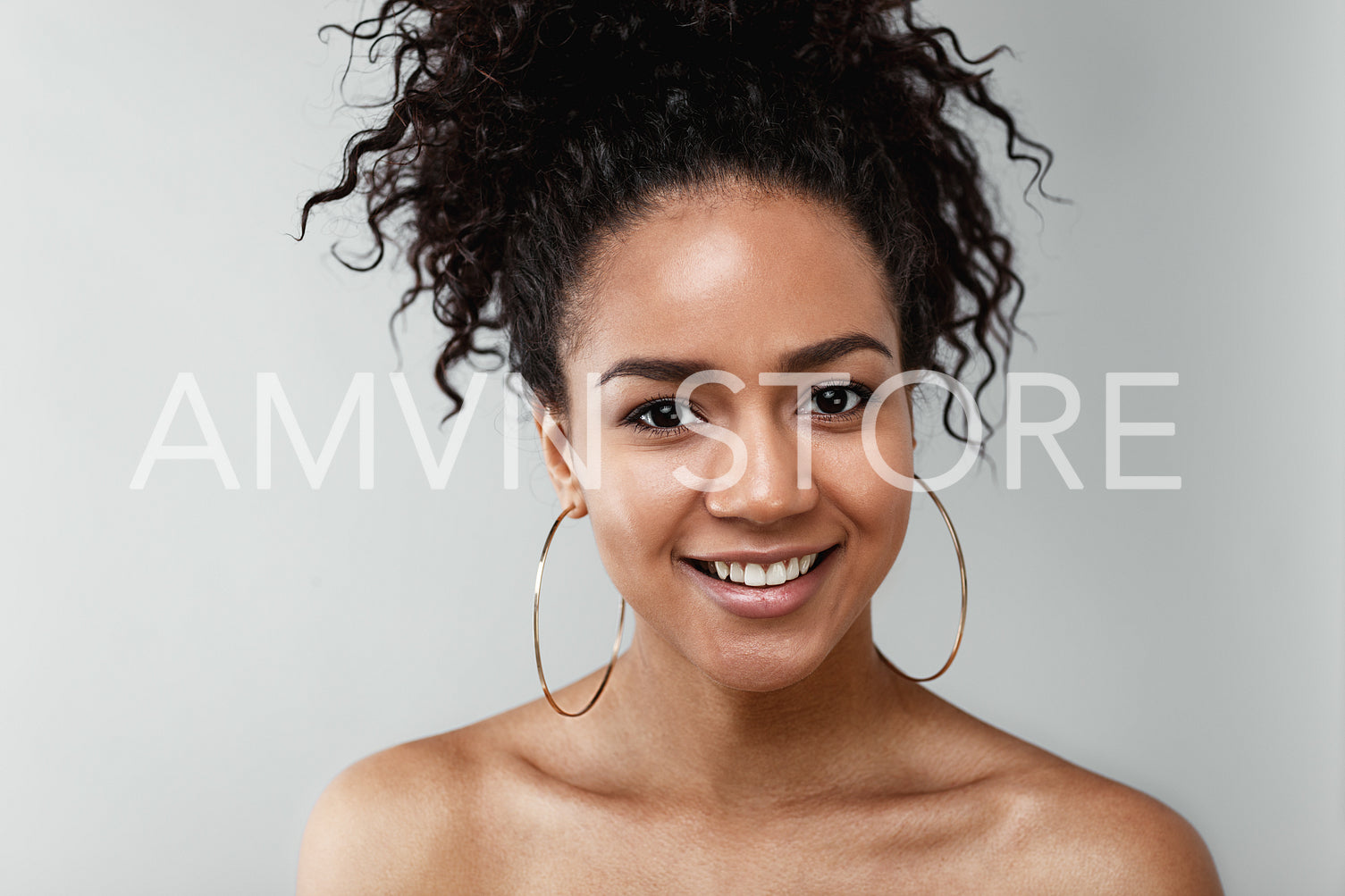 Portrait of smiling young woman with earrings against gray background	