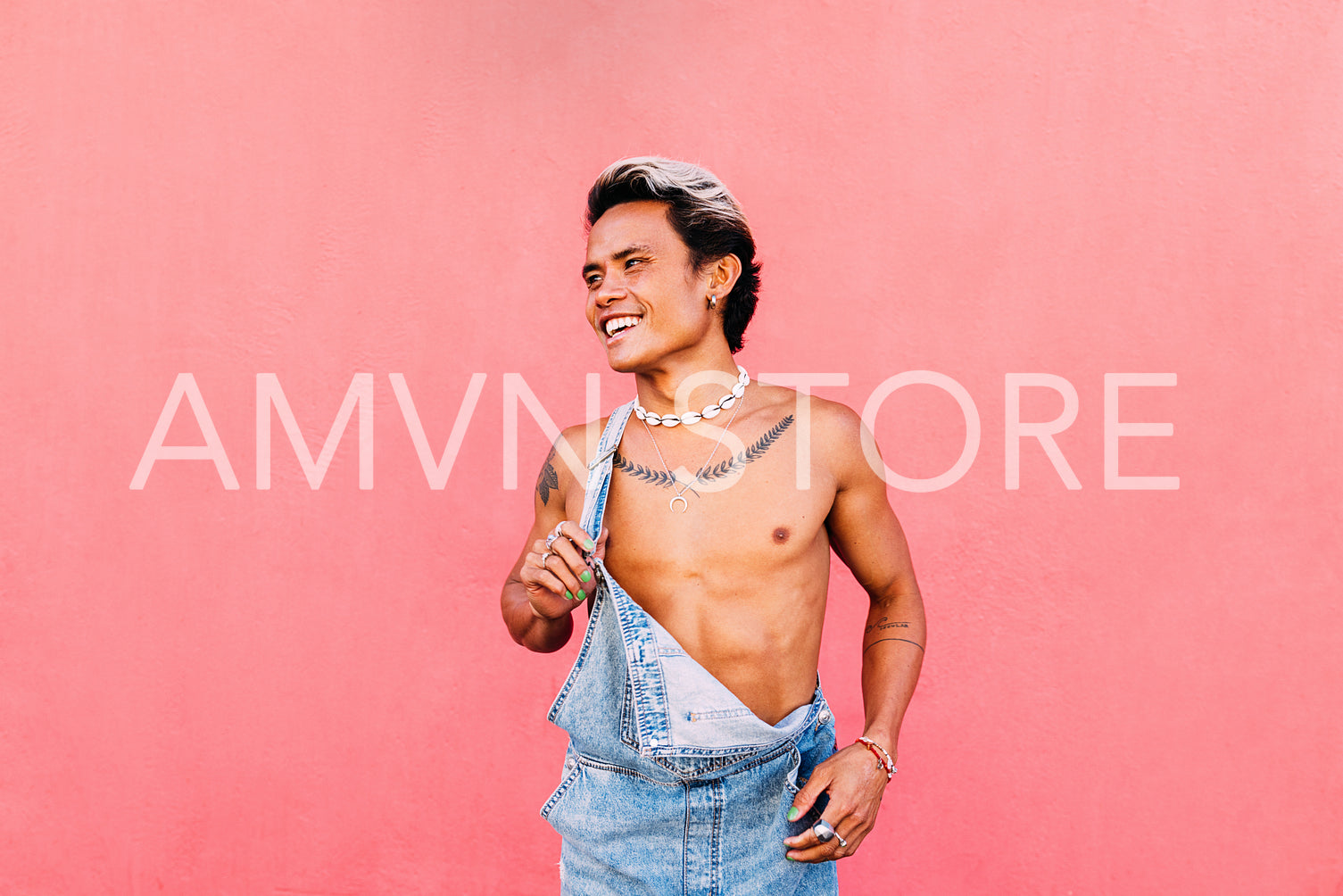 Portrait of a young smiling guy in denim overalls looking away while standing at pink wall