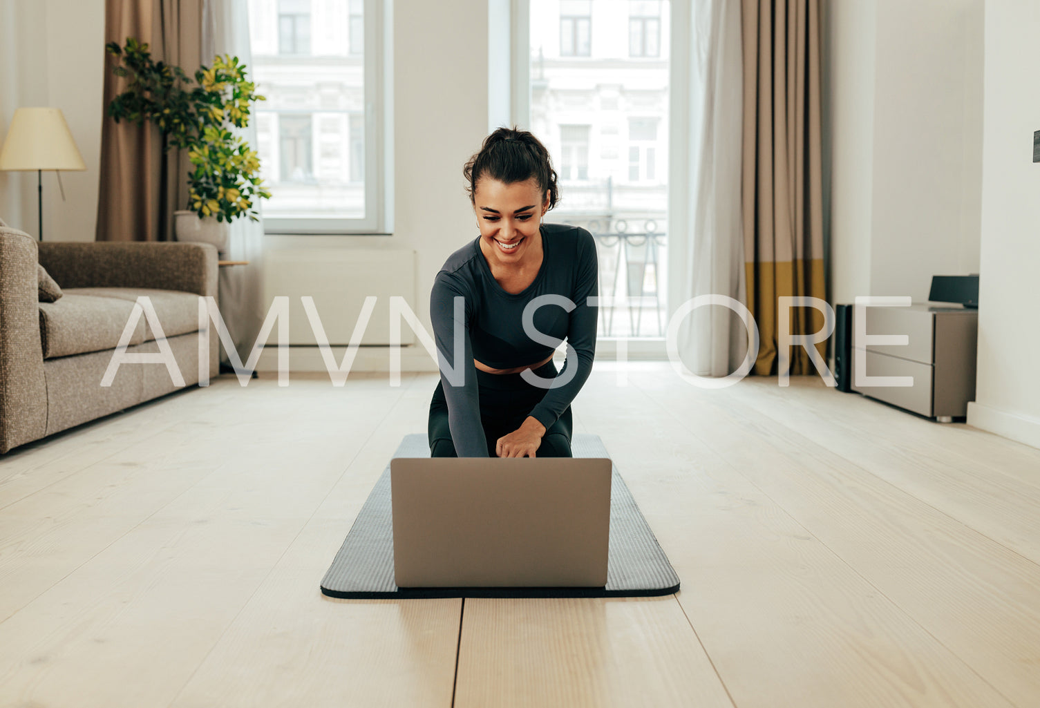 Woman in sportswear sitting on floor and using a laptop. Fitness female preparing for online sport class at home.	