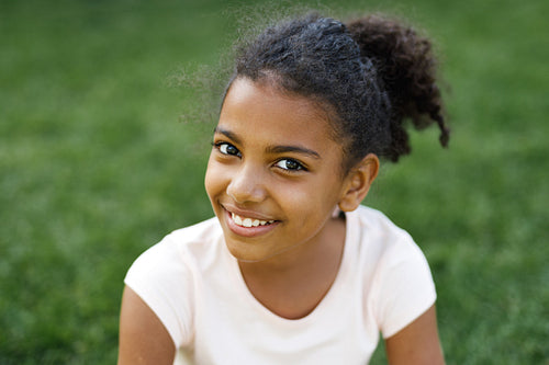 Smiling girl sitting on a grass in park, looking at camera