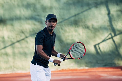 Professional tennis player with racket looking at camera on hard court
