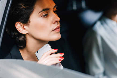 Pensive businesswoman holding a cell phone while sitting in a car