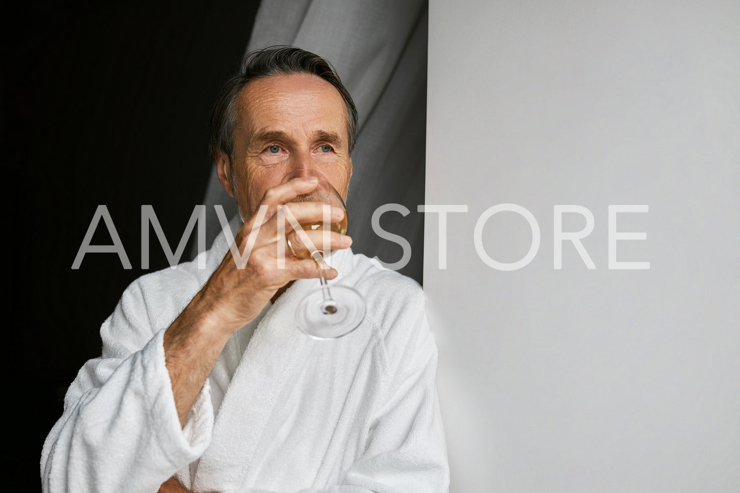 Male relaxing at home. Mature man looking at window and drinking wine.